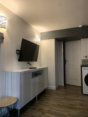 Una cocina moderna con lavadora integrada, un televisor de pantalla plana montado en un mueble blanco y una pequeña mesa redonda.