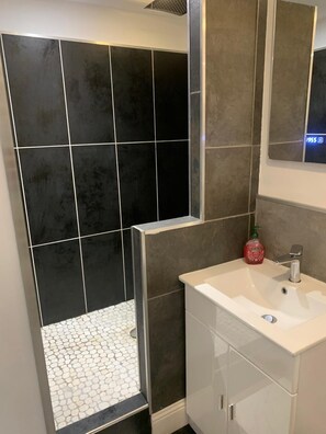 Une salle de bain avec une douche, des murs carrelés, un lavabo et un miroir.