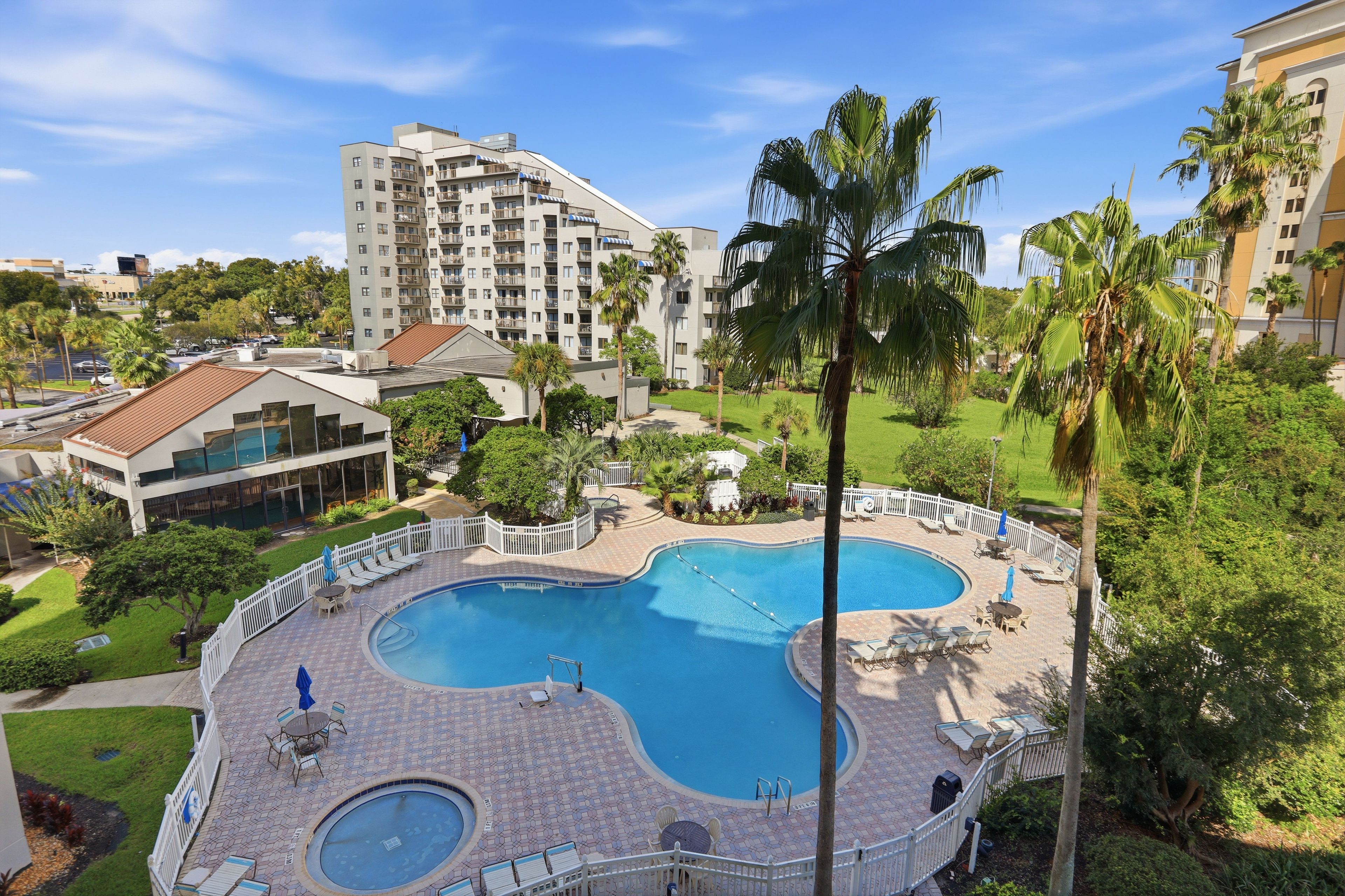 A hotel with a large swimming pool surrounded by lounge chairs and palm trees.