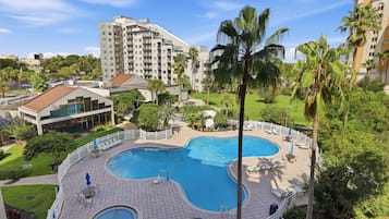 A hotel with a large swimming pool surrounded by lounge chairs and palm trees.