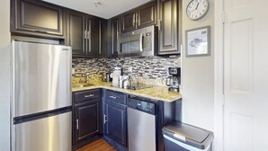Una cocina moderna con electrodomésticos de acero inoxidable, armarios oscuros, salpicadero de azulejos y un reloj en la pared.