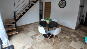 Ein Essbereich mit einem schwarzen Tisch, weißen Stühlen, einer Topfpflanze, einer Uhr und einer Treppe.