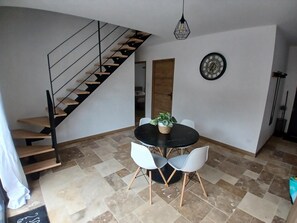 Ein Essbereich mit einem schwarzen Tisch, weißen Stühlen, einer Topfpflanze, einer Uhr und einer Treppe.