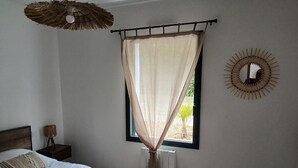 Ein Schlafzimmer mit einem Bett, einem Fenster mit durchsichtigen Vorhängen, einem Wandspiegel und einem Deckenventilator.