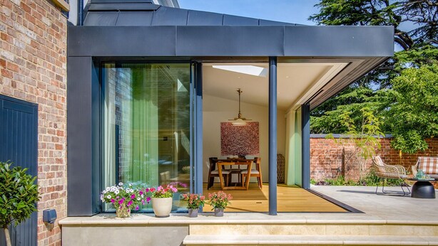 Ein modernes Haus mit einem großen Schiebeglastür, die zu einem Essbereich mit Tisch und Stühlen führt.