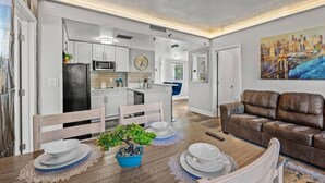 Una cocina moderna con armarios blancos, un refrigerador negro y un comedor con una mesa de madera dispuesta para cuatro.