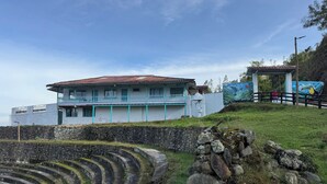 A coastal building with a red-tiled roof, a balcony, and a mural on the adjacent wall.