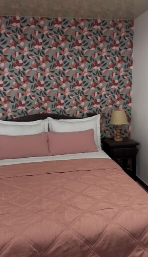 Un lit avec une couette rose, une tête de lit blanche et un papier peint à motifs floraux.