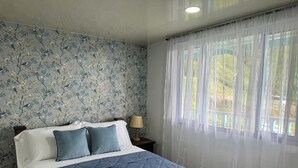 A bedroom with a bed, pillows, a nightstand, a lamp, and a window with sheer curtains.