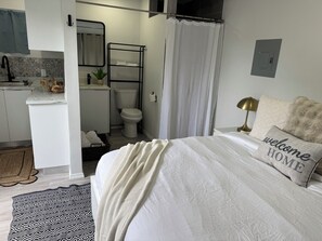 A bedroom with a bed, a bedside lamp, a 'welcome home' pillow, a bathroom with a toilet, a sink, and a shower curtain. - Cozy Hardrock Retreat- Walk to Hardrock Casino! Close drive Beach and Restaurant (Hollywood)