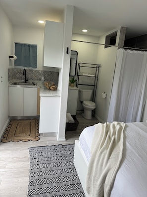 Een kleine kamer met een kitchenette, toilet en een bed.