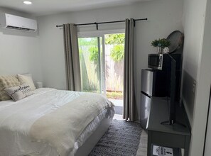 A bedroom with a bed, a TV, a small table, and a sliding glass door leading to a patio.