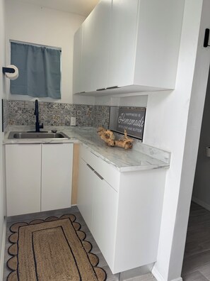 Una cocina compacta con armarios blancos, encimera de mármol, un lavamanos y un letrero decorativo.