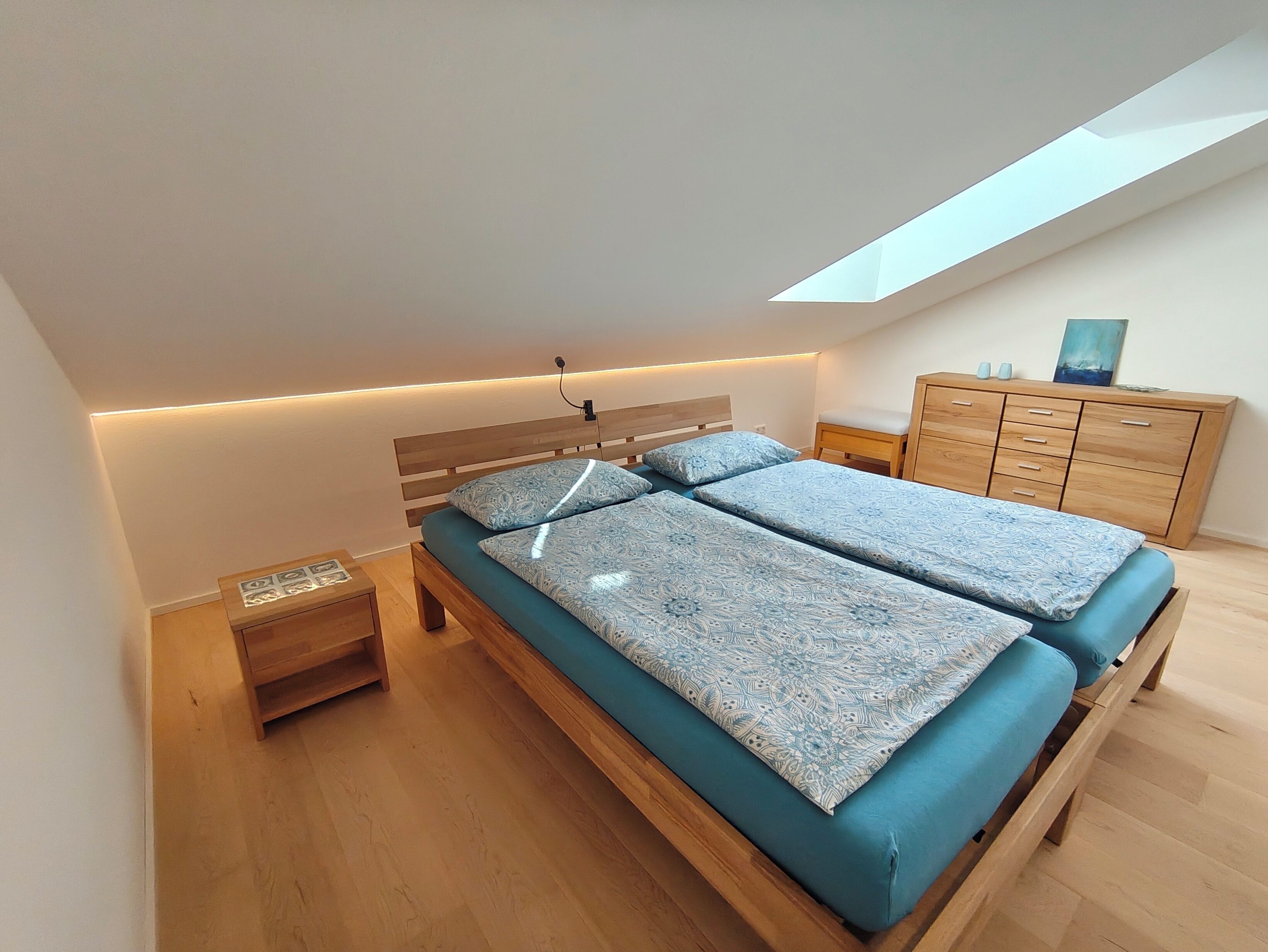 A modern bedroom with a skylight, a wooden bed frame, a bedside table, and a wooden dresser.
