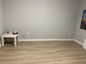 Een kamer met een lichtgrijze muur, een witte tafel met enkele spullen en een houten vloer.