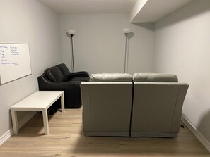 Een kamer met een whiteboard, een zwarte stoel, een beige bank, een witte tafel en twee vloerlampen.