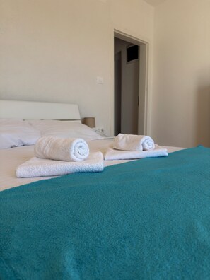 Ein Hotelzimmer mit einem Bett, einer tĂŒrkisnen Tagesdecke und aufgerollten weiĂen HandtĂŒchern.