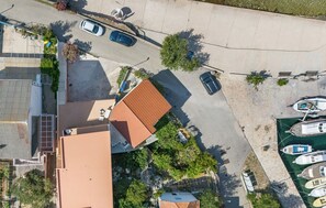 Oversigtsbillede af et boligområde med et hus med rødt tag, parkerede biler og en lystbådehavn med både.