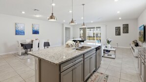 Una cocina moderna con encimeras de granito, electrodomésticos de acero inoxidable, iluminación colgante y un comedor con mesa y sillas.