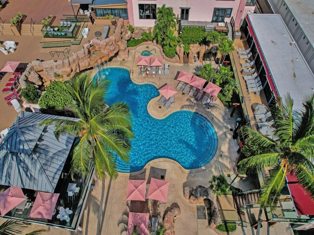 Vista aerea di un resort con piscina centrale, aree relax e palme.