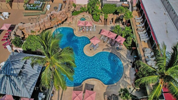Vista aerea di un resort con piscina centrale, aree relax e palme.