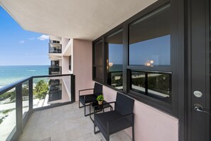 Een balkon met uitzicht op de oceaan, twee stoelen, een kleine tafel en een bloempot.