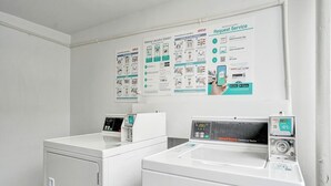 Un'area lavanderia con due lavatrici, un'asciugatrice e manifesti illustrativi appesi al muro.