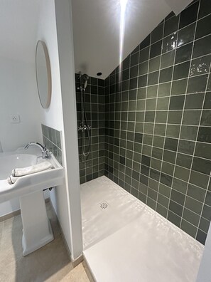 Ein Badezimmer mit einem weißen Waschbecken, einem Spiegel und einer Dusche mit dunkel gefliesten Wänden.
