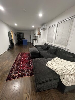 Una sala de estar con un sofá modular, un tapete estampado rojo y una manta tejida blanca.