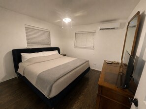 Ein Schlafzimmer mit Bett, Nachttischen, einem Schminktisch und einem Spiegel, sowie einer Klimaanlage.