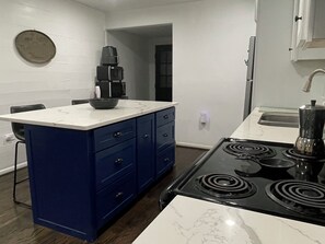 Une cuisine équipée d’une cuisinière, d’un évier, de placards bleus et d’un plan de travail en marbre.