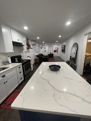 Una cocina moderna con armarios blancos, una isla de mármol y un comedor con alfombra roja.