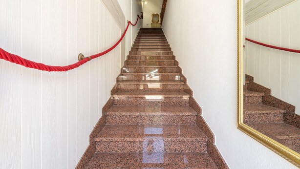 Eine Marmortreppe mit roten Seilen, die zu einem Raum mit einem Spiegel und einem gerahmten Bild an der Wand führt.