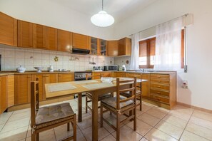 A kitchen with wooden cabinets, a dining table with chairs, a microwave, and a sink.
