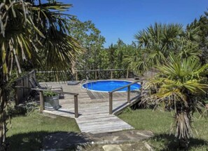 Ein Garten mit Holzterrasse, Pool und üppiger tropischer Bepflanzung.