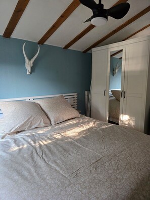 A bedroom with a bed, a ceiling fan, a white wardrobe, and a wall-mounted animal skull. - Vrbo Property (Salavas)