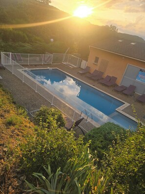 A swimming pool with a fenced deck, lounge chairs, and a building with a sign. - Vrbo Property (Salavas)