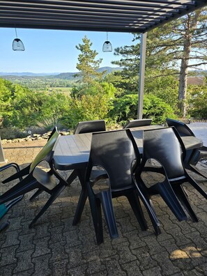 An outdoor patio with a table and chairs, a pergola overhead, and a scenic view of trees and hills. - Vrbo Property (Salavas)