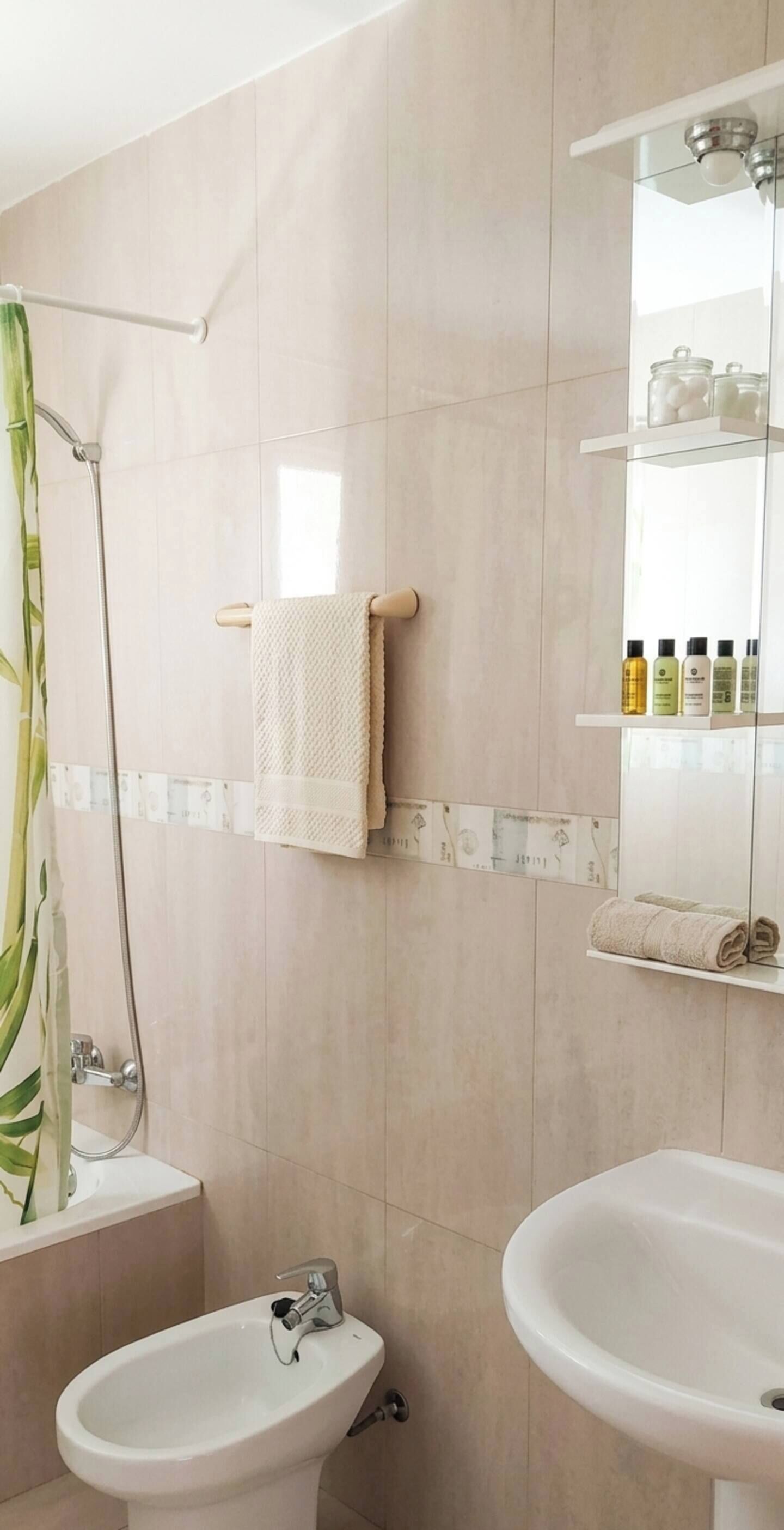 A bathroom with a shower, two sinks, a towel rack, and a shelf with toiletries.
