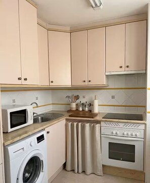 A compact kitchen with a washing machine, microwave, stove, and sink.