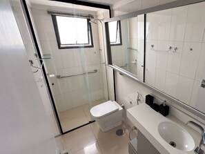 Un bany modern amb una cabina de dutxa de vidre, un vàter blanc, un lavabo amb un mirall damunt i un terra emblat.