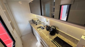 A compact kitchen with a stainless steel sink, a coffee machine, and a toaster.