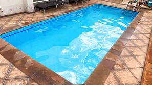 Piscina retangular com água azul cristalina, ladeada por ladrilhos de pedra.