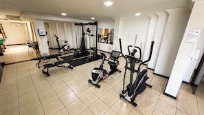 A gym with various exercise equipment, a bench, and a mirrored wall.