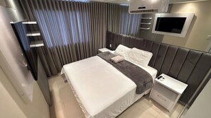 Quarto de hotel moderno com cama, mesa de cabeceira, televisão e ar condicionado.