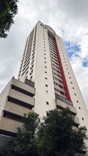 Um edifício alto e moderno, com vários andares, janelas grandes e uma faixa vermelha vertical marcante.