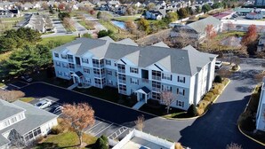 Un immeuble résidentiel à plusieurs étages, doté d’un parking, entouré d’autres maisons.