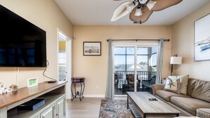 Un salon avec un téléviseur, un canapé, une table basse et une vue sur l’extérieur, visible à travers une porte vitrée.