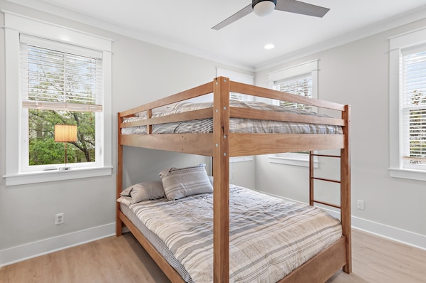 Ein Stockbett in einem Raum mit weißen Wänden, einem Deckenventilator und Fenstern mit Jalousien.