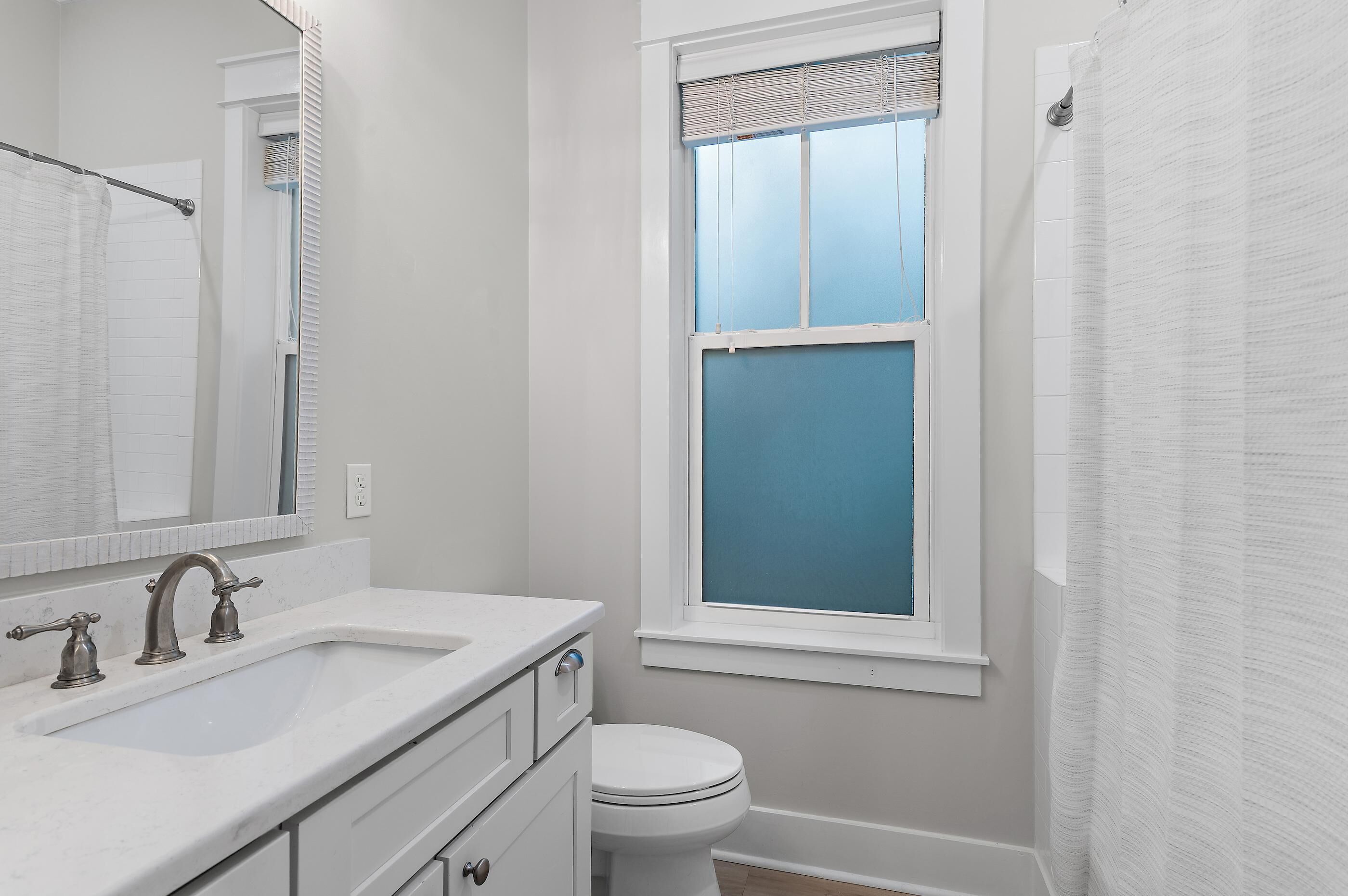 A bathroom with a white sink, a toilet, a window with blinds, and a shower curtain.